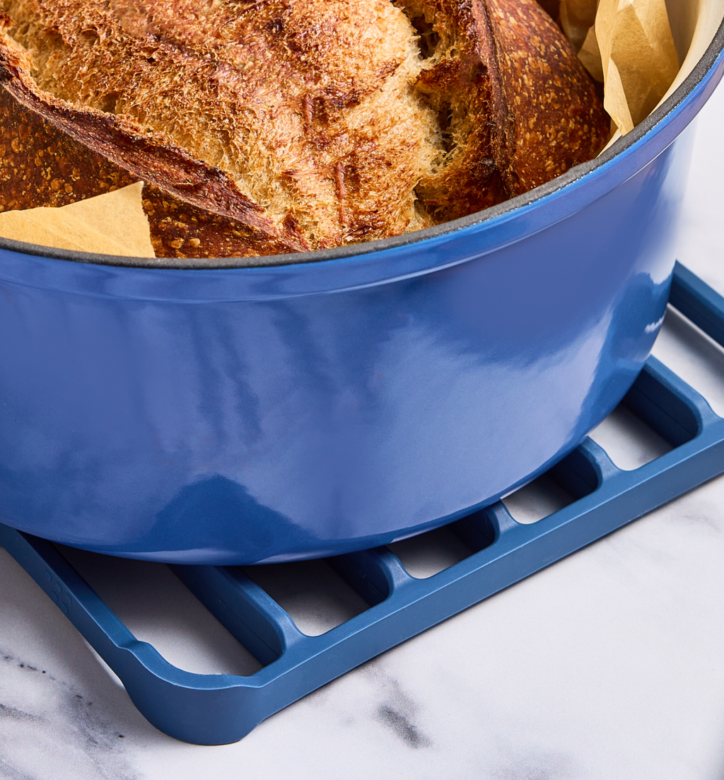 Freshly baked sourdough bread in a blue enameled cast iron Dutch oven on a matching trivet